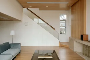Modern living room with a wooden staircase, glass railings, and a wooden floor.