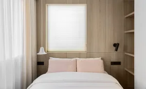 A minimalist bedroom with wooden walls, a white bed, and pink pillows.