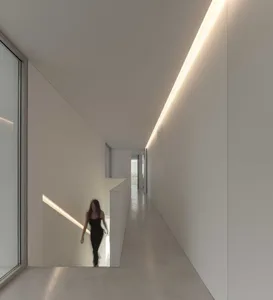 A modern minimalist interior with concrete walls and flooring, featuring a person walking down a white stairwell.
