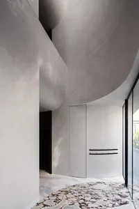 A minimalist space featuring concrete walls and a marble floor, with a curved ceiling and spacious layout.