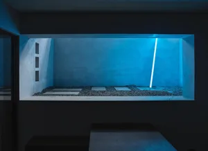 Modern minimalist interior with a concrete floor, concrete walls, and a blue light fixture.