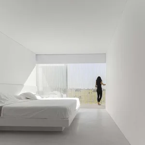 A modern bedroom with white walls and a glass window providing a view of the outdoors.