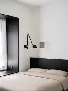 A modern bedroom with a minimalist design featuring black and white tones, a black headboard, beige bedding, and a wall-mount