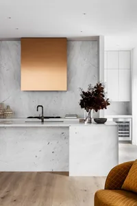 A modern kitchen with minimalist design, featuring marble countertops and a gold-hued backsplash.