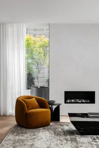 A modern living room with a minimalist design featuring a mustard-colored chair, a black marble coffee table, and a large win