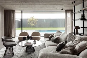 Modern living room with fabric furniture, minimal decor, and large glass windows overlooking a pool.