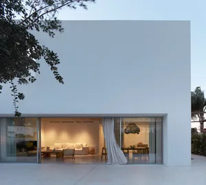 Modern minimalist residential interior featuring concrete and glass walls with white furniture.