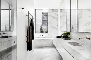 Modern minimalist bathroom with white marble tiles and a large window overlooking an outdoor garden.