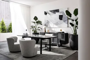 A modern home office with a sleek, black desk, grey upholstered chairs, and a large abstract painting on the wall.
