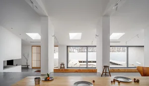 Modern minimalist living room featuring concrete floors, wooden furnishings, and large glass windows.