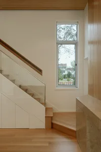 Modern staircase with wooden steps and railings, featuring a tall window with a view of trees.