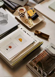 A stack of papers and a desk setup with various objects such as a cup of matches, a small container of matches, a black and w