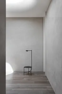 A minimalist metal floor lamp in a modern, empty room with light-colored wooden flooring and textured walls.