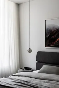 A minimalist bedroom featuring a bed with grey textiles and a glass pendant light hanging from the ceiling.