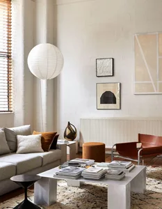 A modern minimalist living room with a white sofa, a coffee table, and various decorative elements including a hanging light 