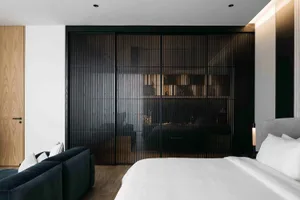 A modern minimalist bedroom featuring a metal wall, a bed with white sheets and gray headboard, and a large sofa with white p