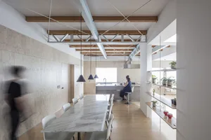 A modern minimalist dining kitchen with a white marble table and chairs, wooden flooring, and exposed wooden beams on the cei