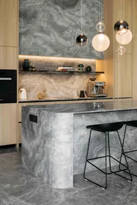 A modern minimalist kitchen with a marble island and countertop, featuring sleek wooden cabinets and pendant lights.