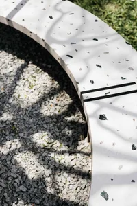 Modern outdoor lounge furniture featuring a white concrete bench with black and grey granite speckles and black metal accents