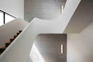 A modern concrete staircase with a wavy design, adorned with natural leaves scattered along the steps and landing.