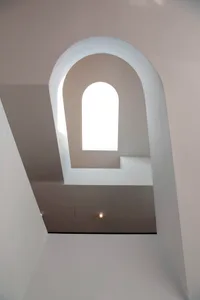 White arch-shaped stairwell with a bright window at the center.