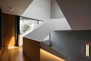 A modern staircase with concrete steps, illuminated by warm lighting, against a backdrop of walnut flooring.