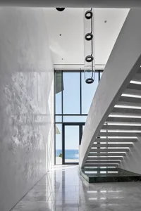Modern minimalist staircase with marble steps and glass railings overlooking the sea.