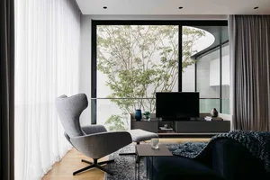 A modern minimalist living room featuring gray fabric furniture, a large glass window, and a glass coffee table.