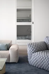A minimalist living room with a beige sofa, a gray textured armchair, and a glass top table.