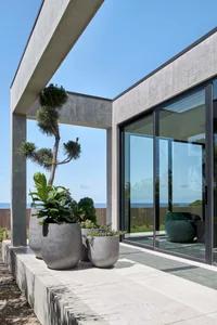 Concrete planters with green plants on a modern exterior patio with glass walls and concrete flooring.