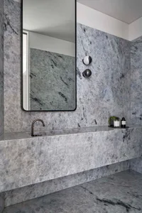 A modern bathroom with marble walls and floor, featuring a floating vanity with a black faucet and a large rectangular mirror