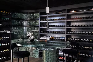 A modern wine cellar with a marble bar, shelves full of wine bottles, and stools.