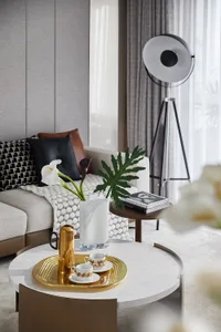 A modern living room with a white marble coffee table adorned with a gold tray containing cups and saucers, a gold vase, a wh