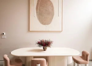 Minimalist dining room featuring an oval wooden table and contemporary chairs, with a floral centerpiece and abstract artwork