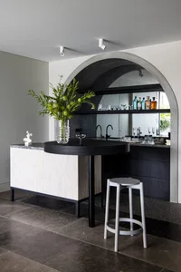 A modern bar counter made of concrete with a vase of greenery and a stool.
