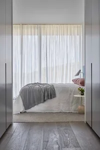 A modern minimalist bedroom with a bed, curtains, and a side table.