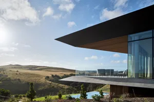 A modern house with a glass exterior overlooking a hilly landscape.