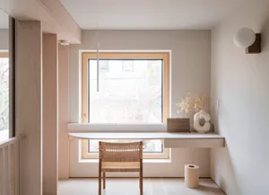 A minimalist home office with a small white desk, wooden chair, and a vase of flowers.