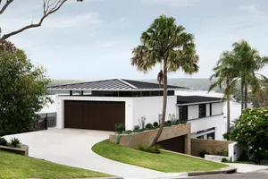 A modern house with a concrete exterior, featuring a large driveway and palm trees.