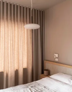 A minimalist bedroom with neutral textiles, wood accents, and a glass pendant light.