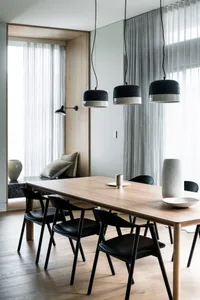 A modern dining room featuring wooden furniture, black chairs, and hanging pendant lights.