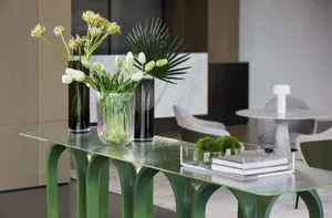 A modern, green console table with glass vases containing flowers and greenery on top of it.