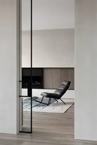 A modern minimalist living room with a black leather lounge chair, wooden flooring, and a rug.