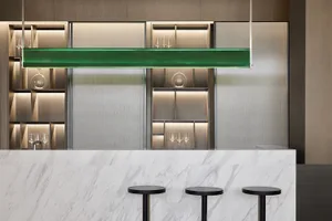 A modern bar counter featuring a green glass shelf, marble counter surface, and glass and metal accents.
