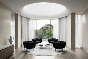 A modern living room with black armchairs, a round coffee table, and a large round rug with large windows and sheer curtains 