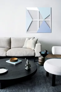 Modern living room with geometric art, round black coffee table, white ottoman, and grey sofa with patterned cushions.