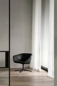 Modern minimalist living room with natural wood flooring and furniture, featuring a sleek, black lounge chair.