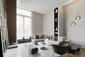 Modern minimalist living room with grey sectional sofa, round coffee table, green chair, and large windows.