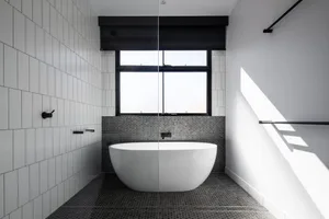Modern minimalist bathroom with a freestanding bathtub, white tiled walls, and black textured walls and floor.