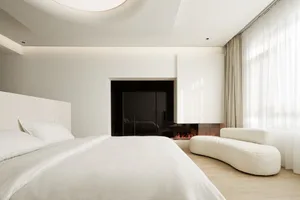 A minimalist bedroom with a white bed, white sofa, and a fireplace with a glass door.